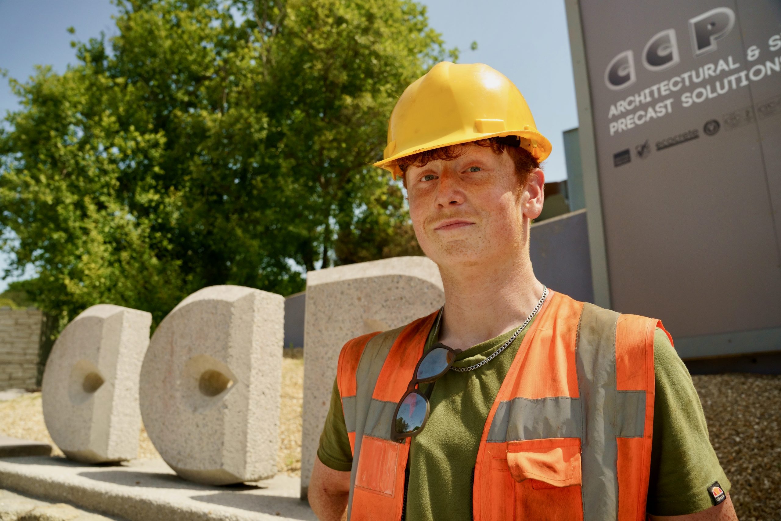 Person wearing a hi-vis and a hard hat in front of some stone sculptures 