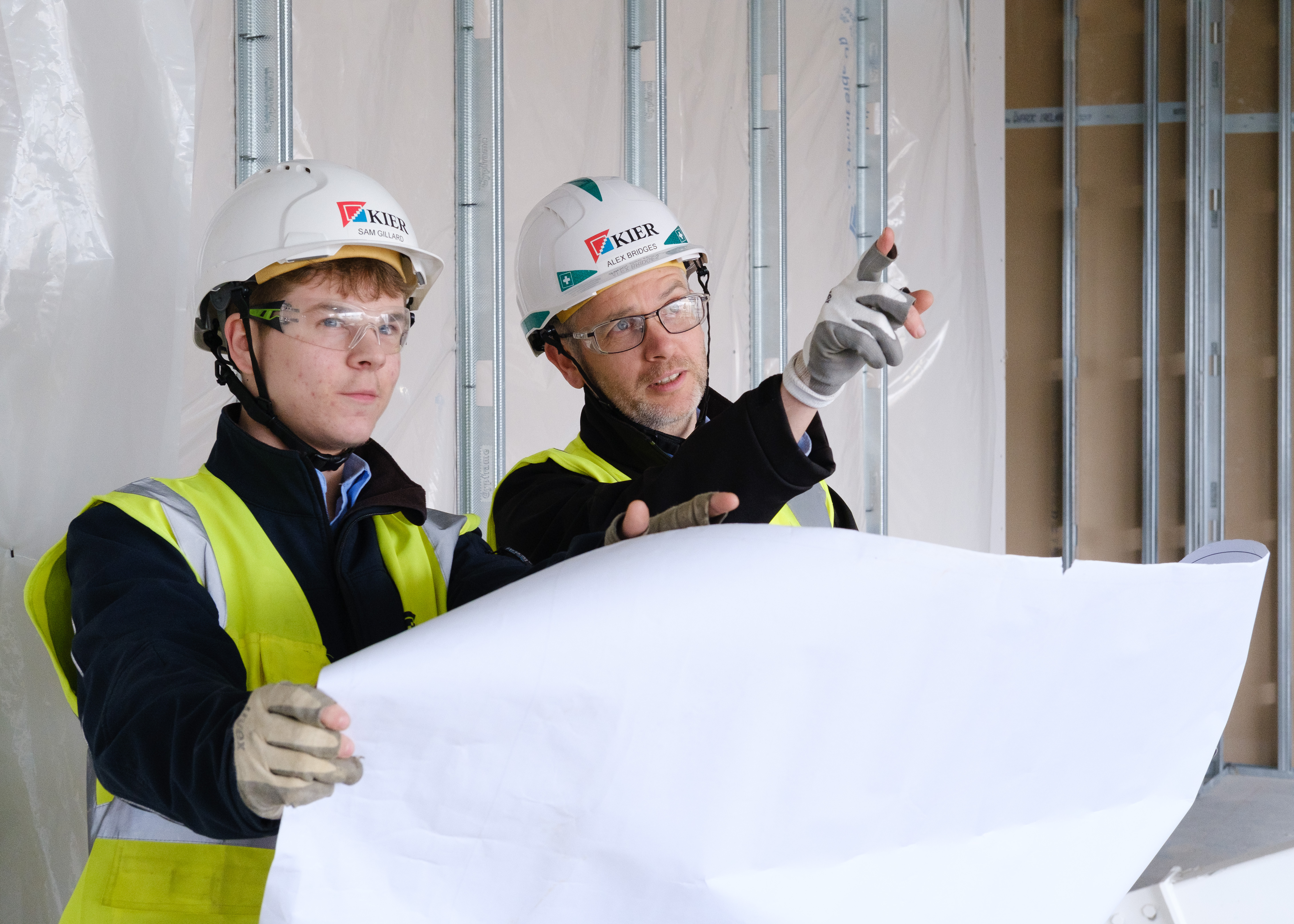Two people wearing hard hats looking at plans and pointing 