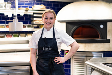 Student chef stood by a wood fired pizza oven