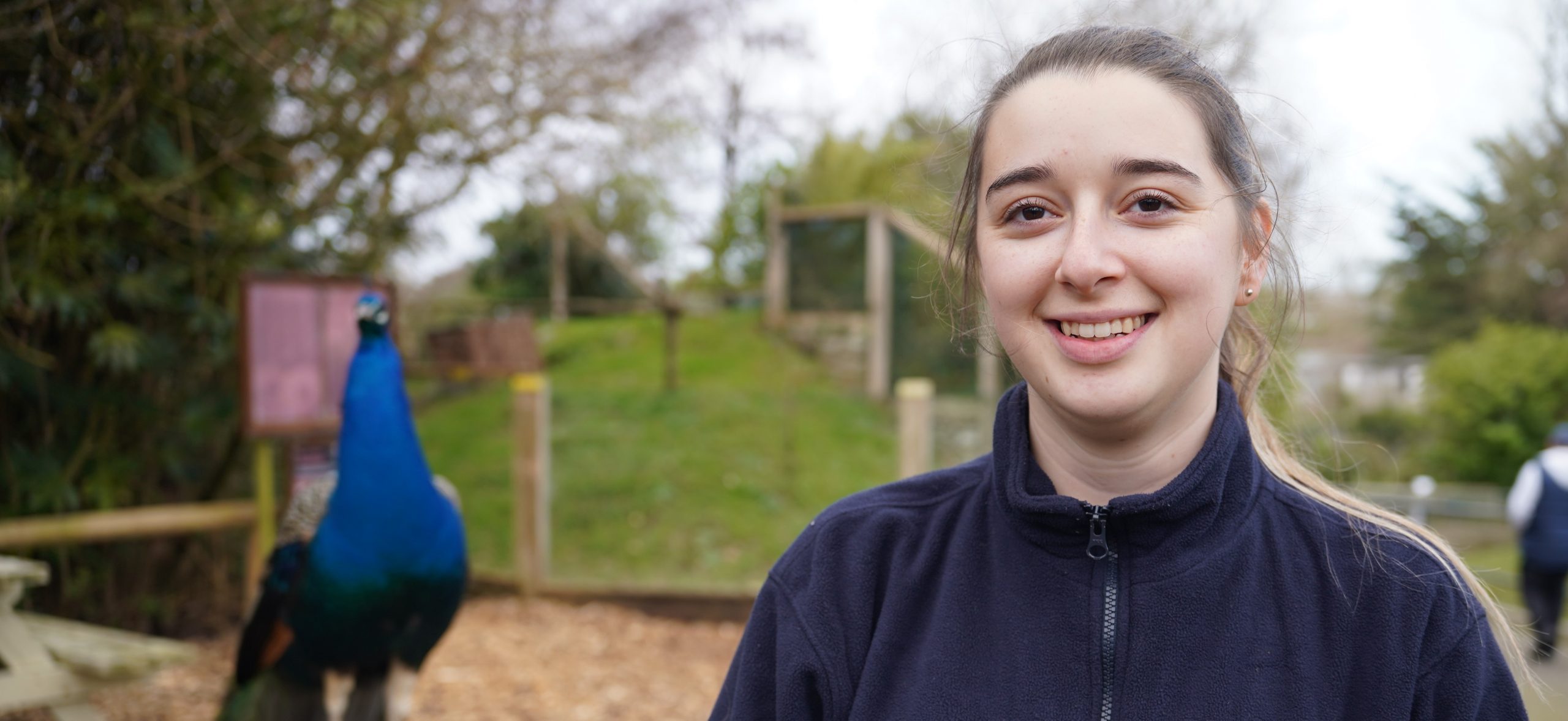 Isobel Hockaday smiling at camera with peacock in the background