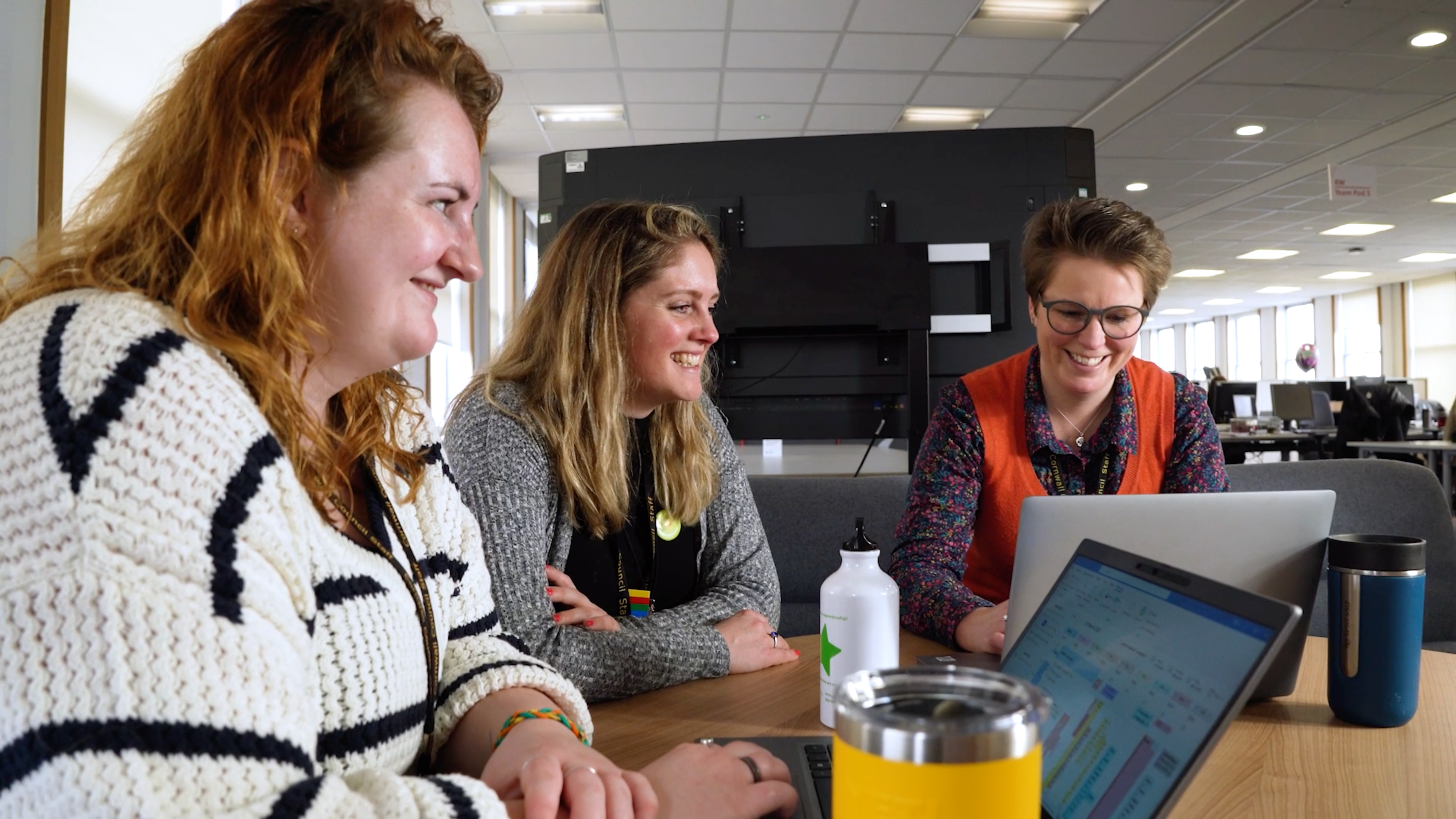 Three people sat together looking at laptops and smiling