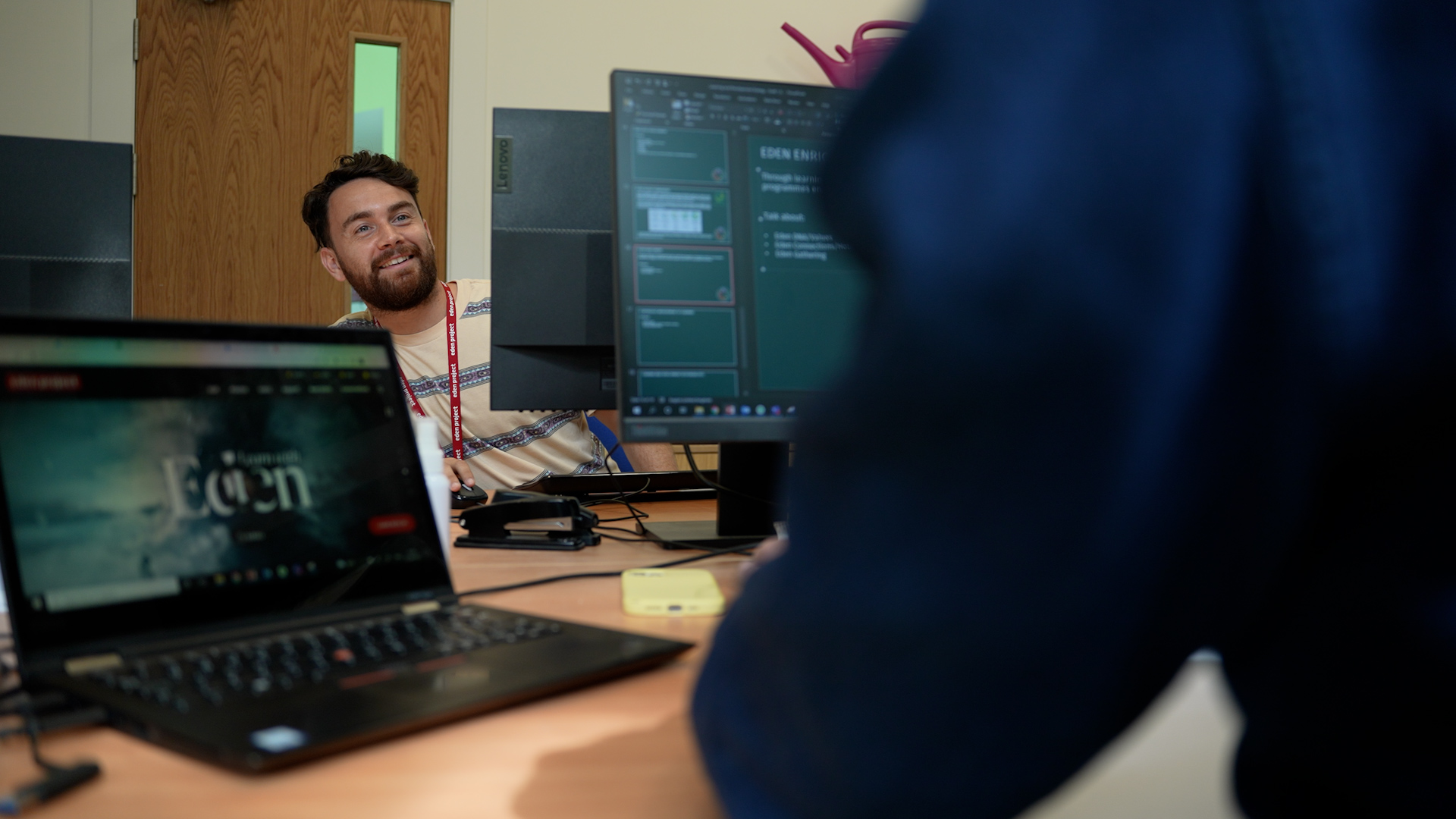 Person working for Eden Project in an office looking round his screen at his colleague